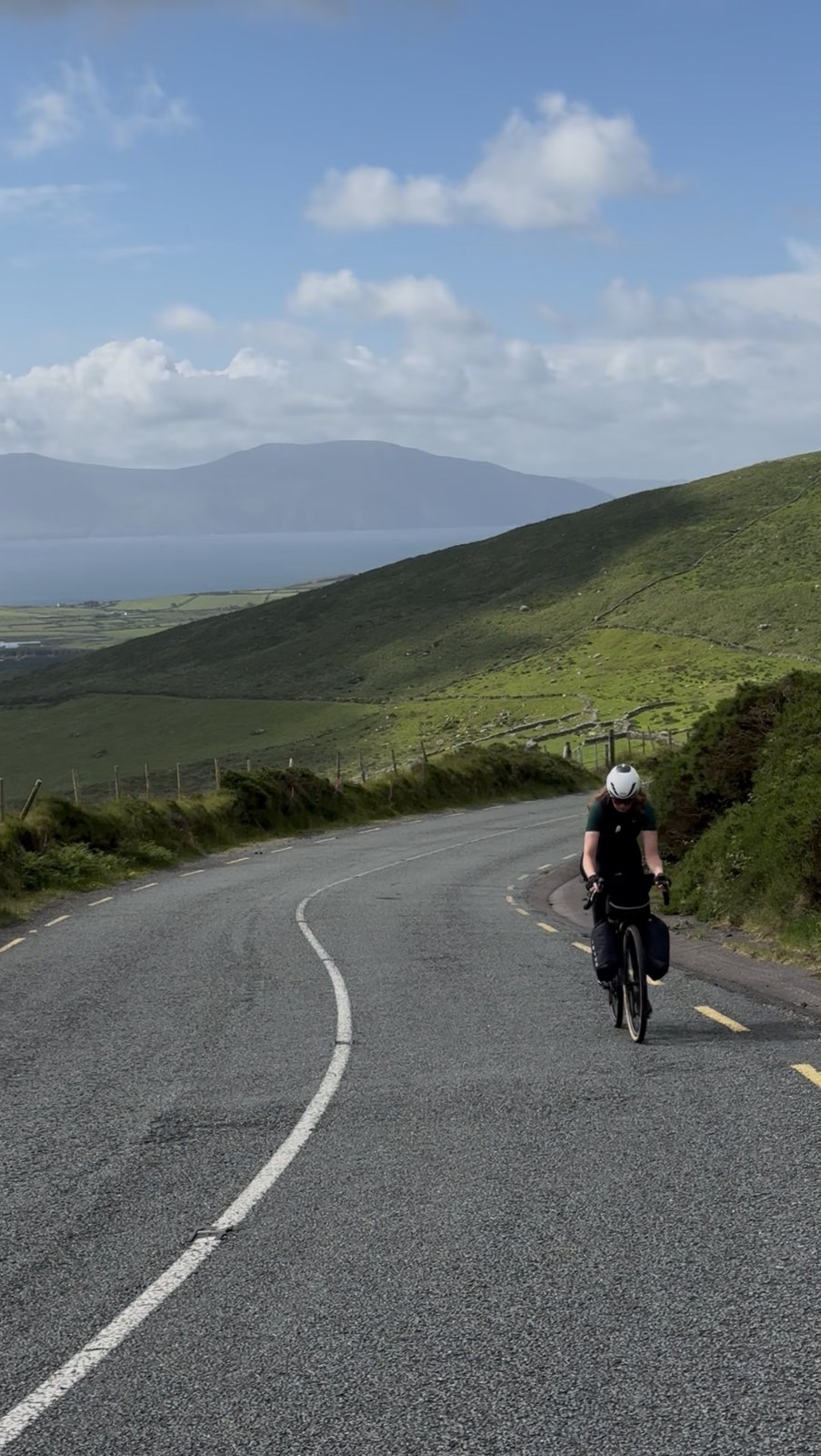 A rider dropping down a curving road toward Dingle Bay and the far mountains