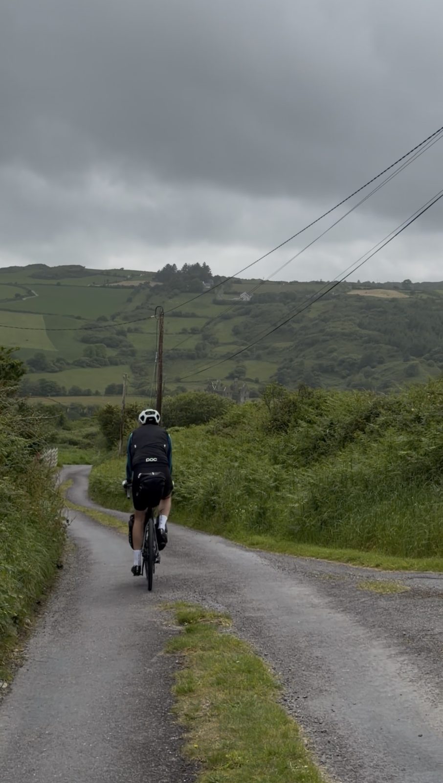 A rider climbing a narrow green country lane in West Cork with a ruined tower in the distance
