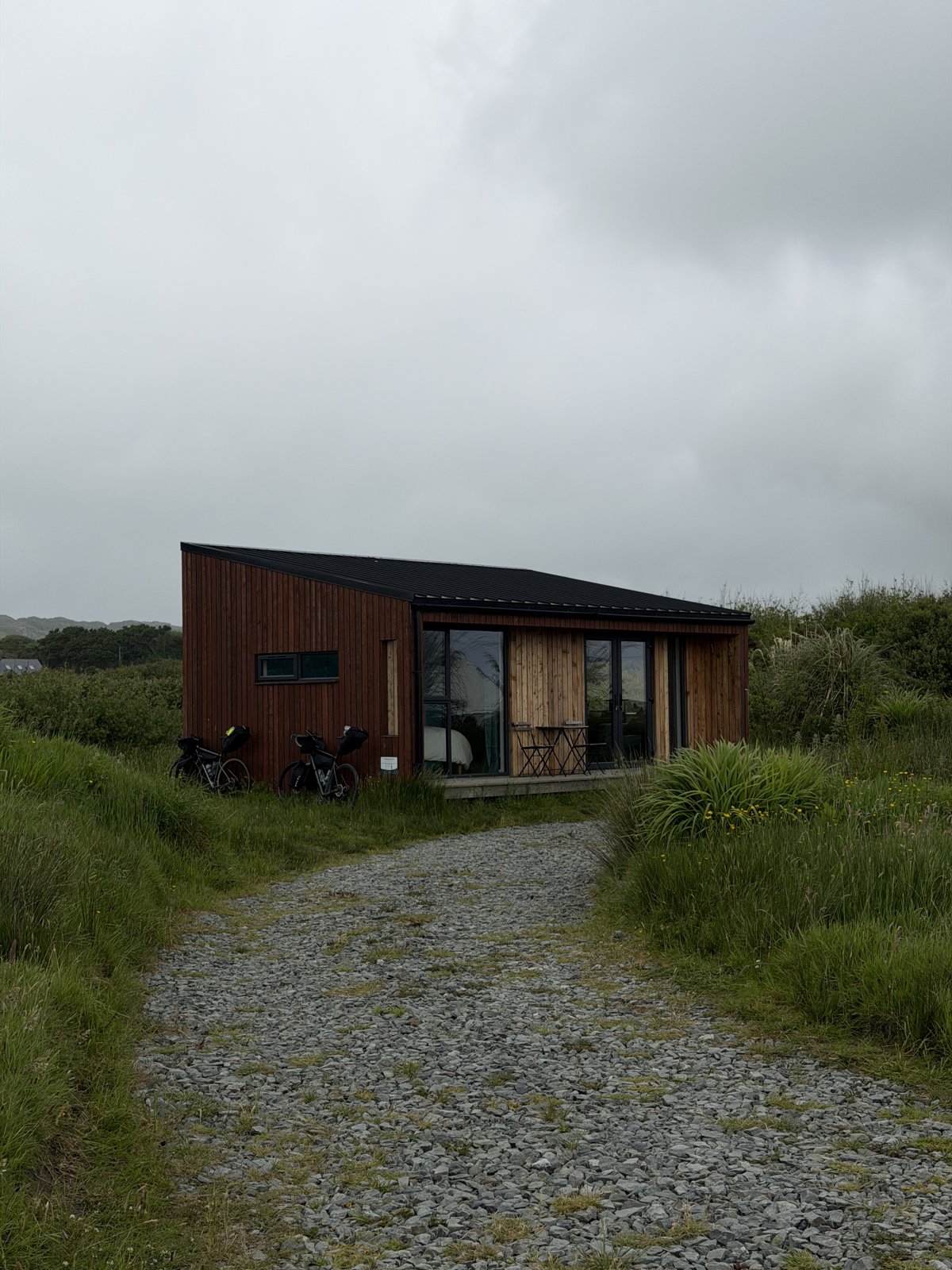 The timber eco cabin at Goleen Harbour with the two loaded bikes parked at the door, up a gravel path through long grass