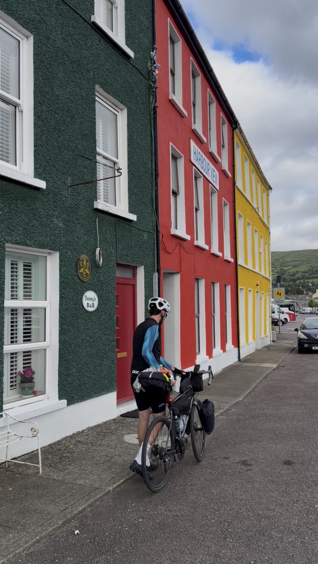 Francis wheeling his loaded bike along the colourful harbour-front terrace in Bantry, past Barry's B&B and the red and yellow houses beside it