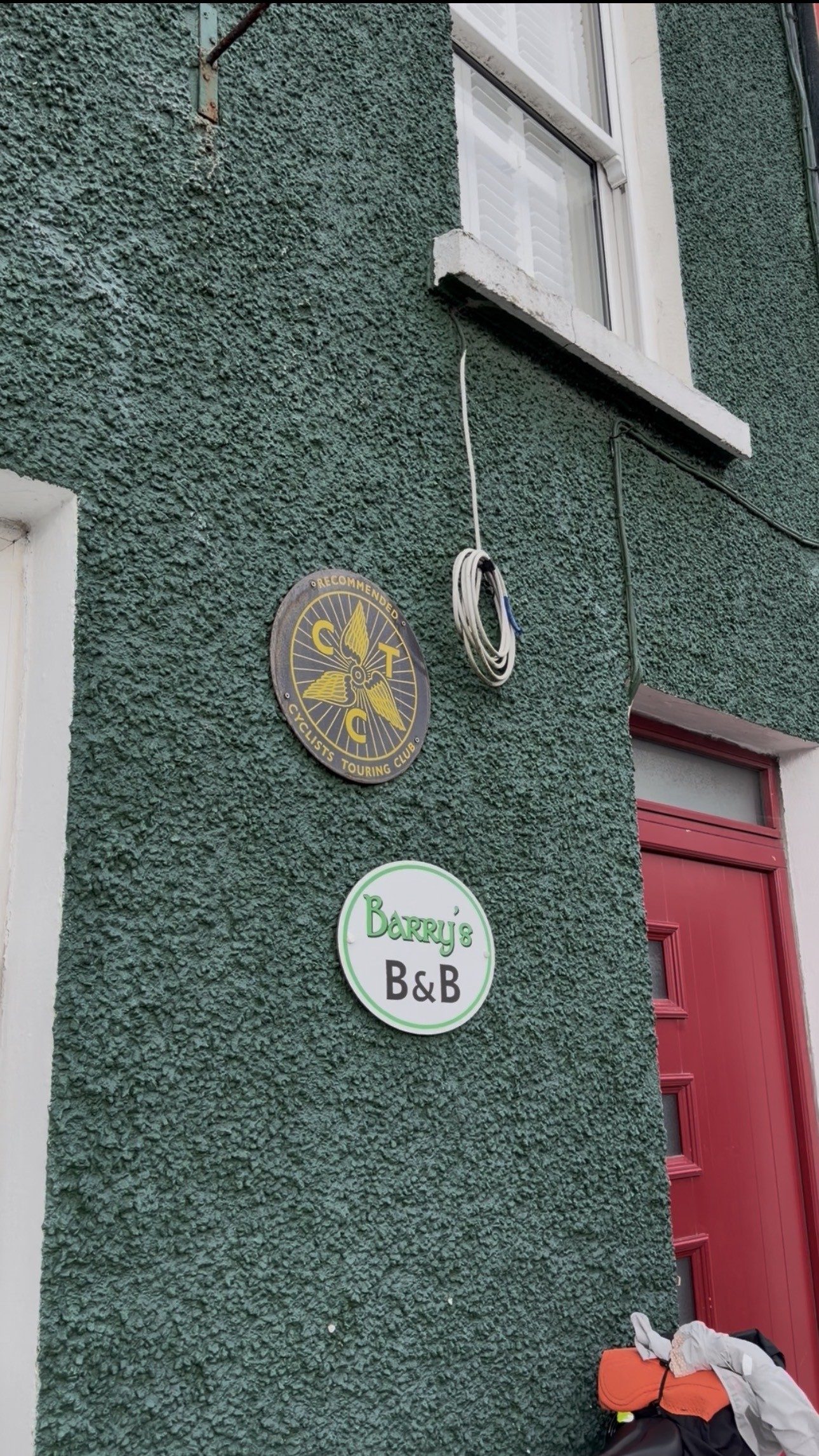The Barry's B&B sign and a cycling club plaque on the green roughcast front wall of the house