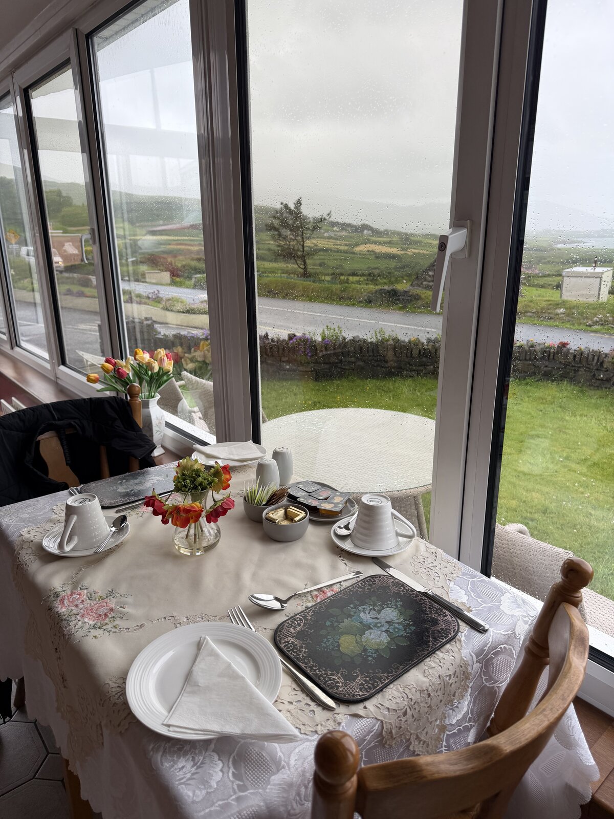 The sun-lounge breakfast table set with tulips and white china, wide windows looking over green fields to Coulagh Bay