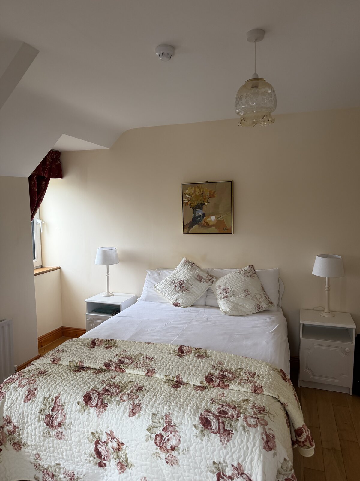 A cosy double bedroom with a floral quilt, bedside lamps and a framed print