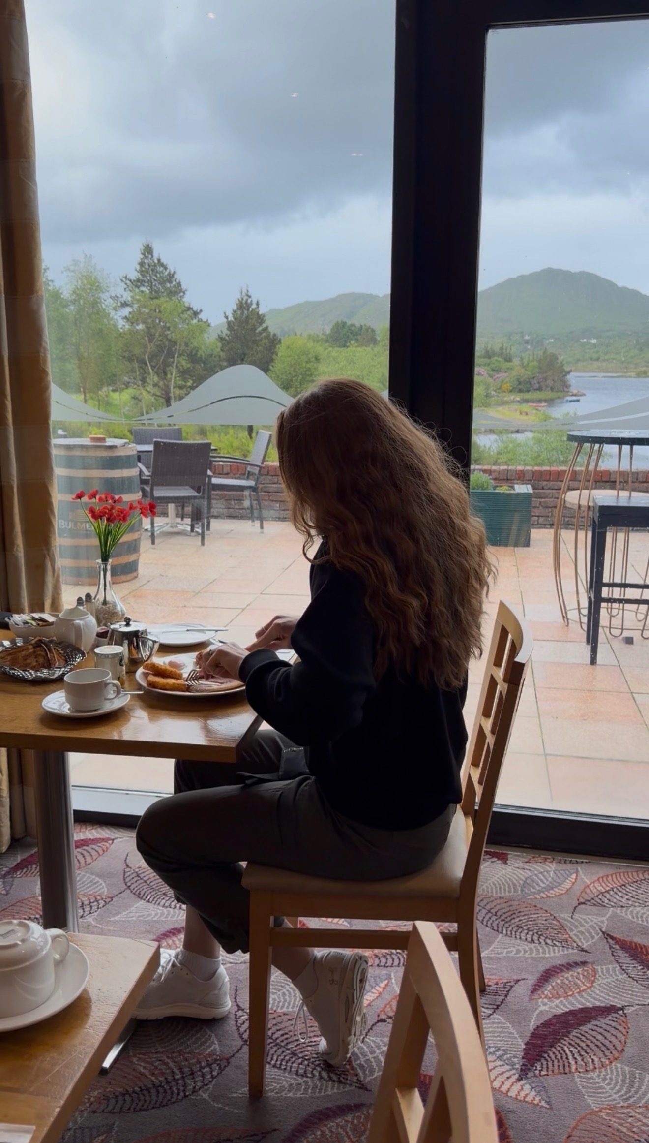 Bailey at a window table eating breakfast, the bay, hills and a barrel of tulips through the glass