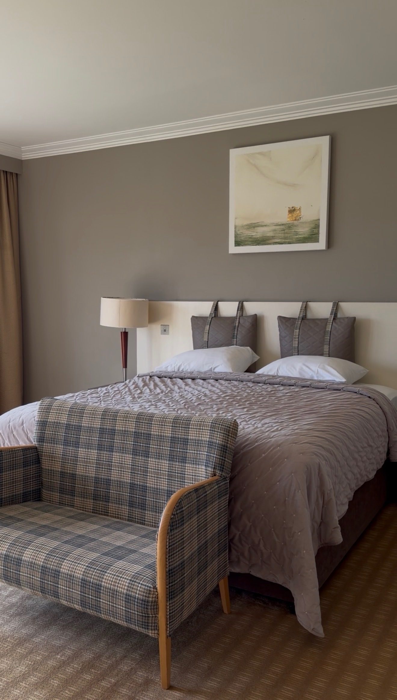 A comfortable double bedroom at the Sneem Hotel with a grey quilt, tartan chair and framed print