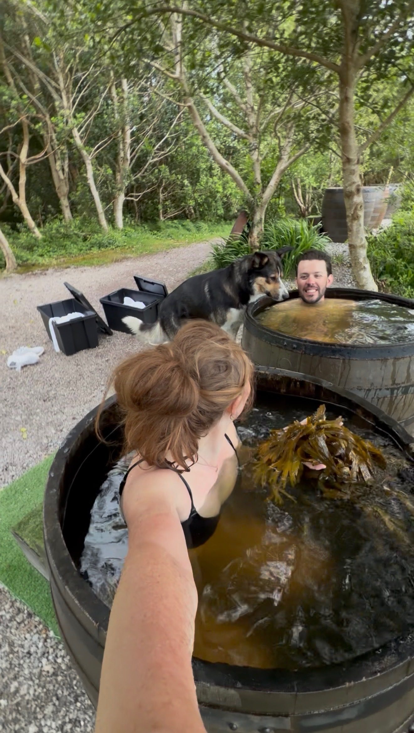 Francis and Bailey soaking in whiskey-barrel seaweed baths in a grove of trees at the Sneem Hotel, their dog Milo alongside