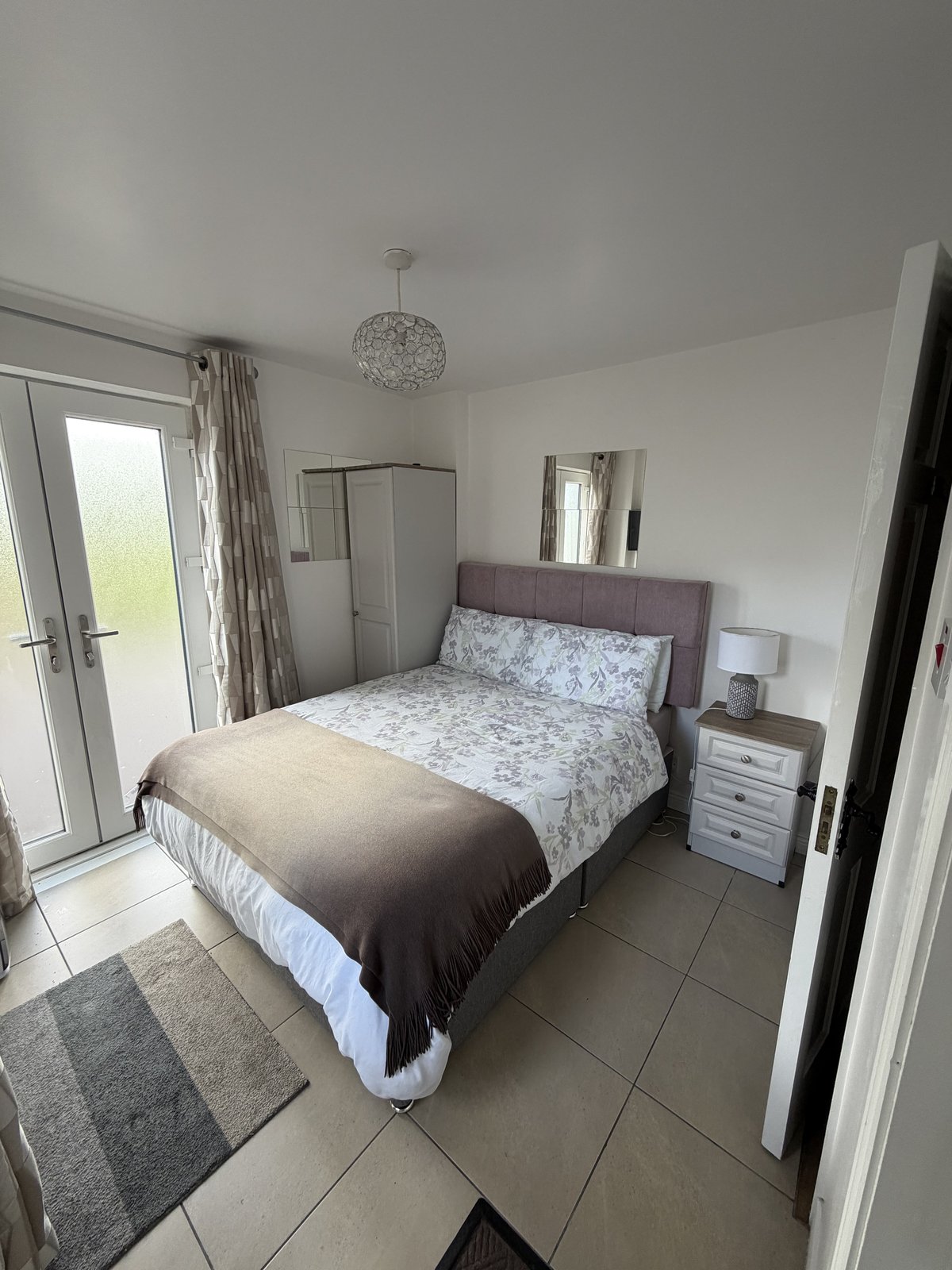 A private double room at Síve Hostel with floral bedding, french doors to the garden and a tiled floor