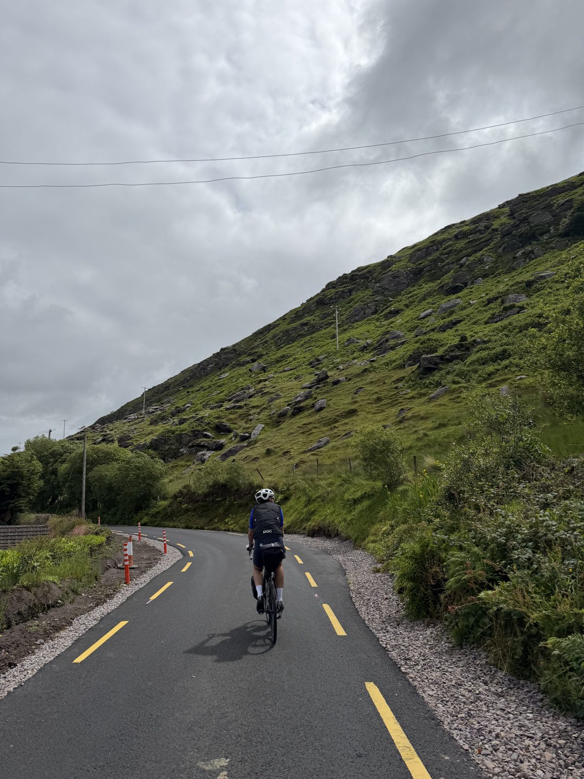 A rider climbing a road below a green and rocky Kerry hillside