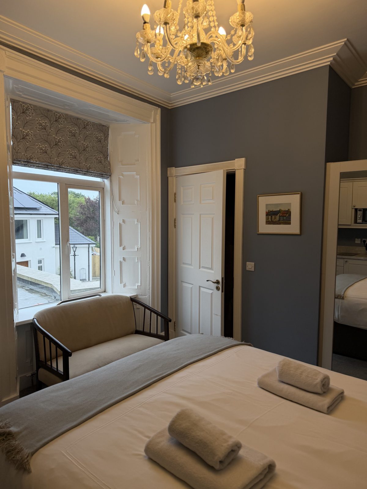 A bedroom at Áras de Staic in Dingle with grey walls, a crystal chandelier and a bright window seat looking onto Green Street