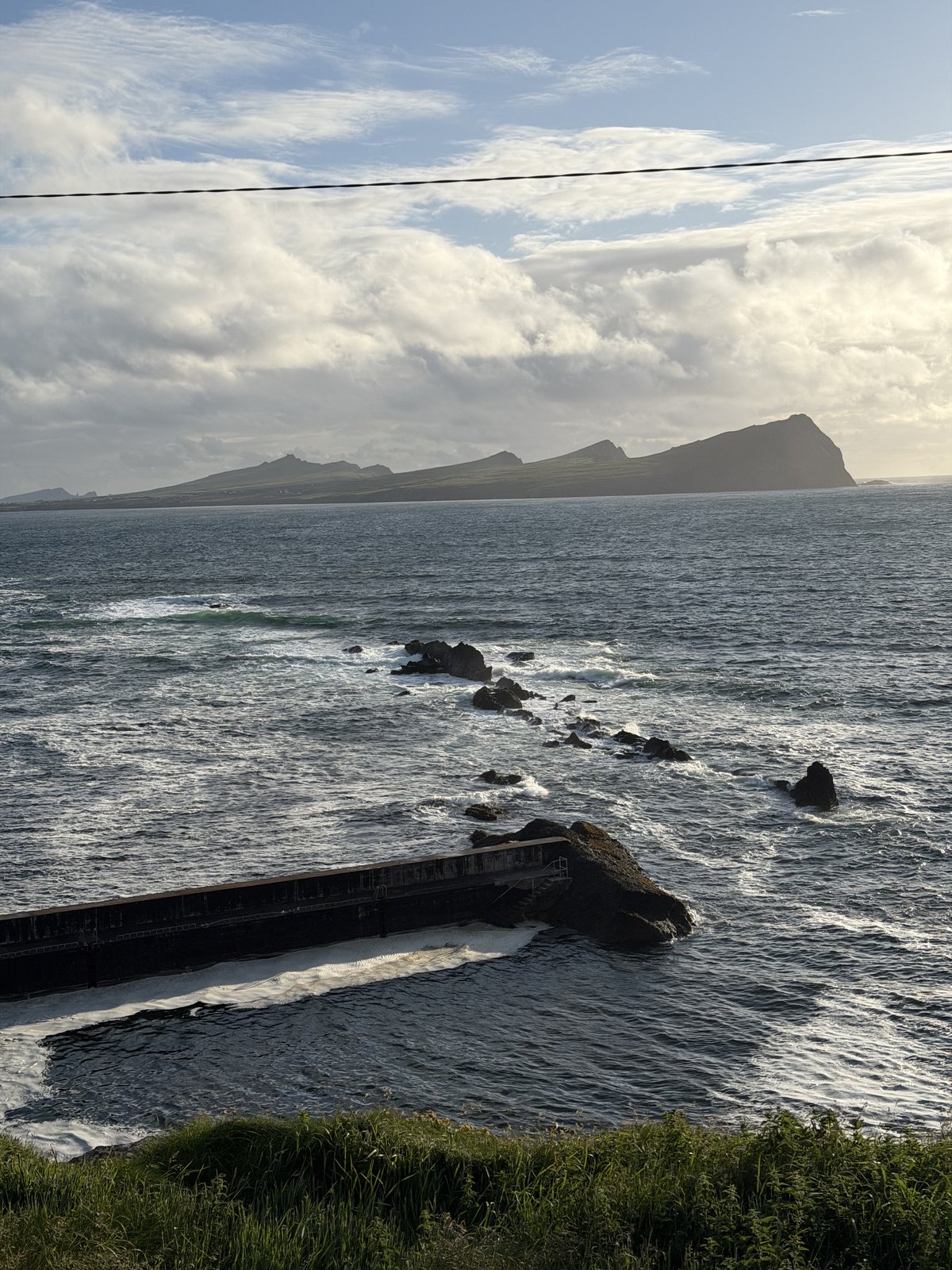 Late golden light over the Atlantic off Slea Head, waves breaking around dark rocks with the headlands beyond