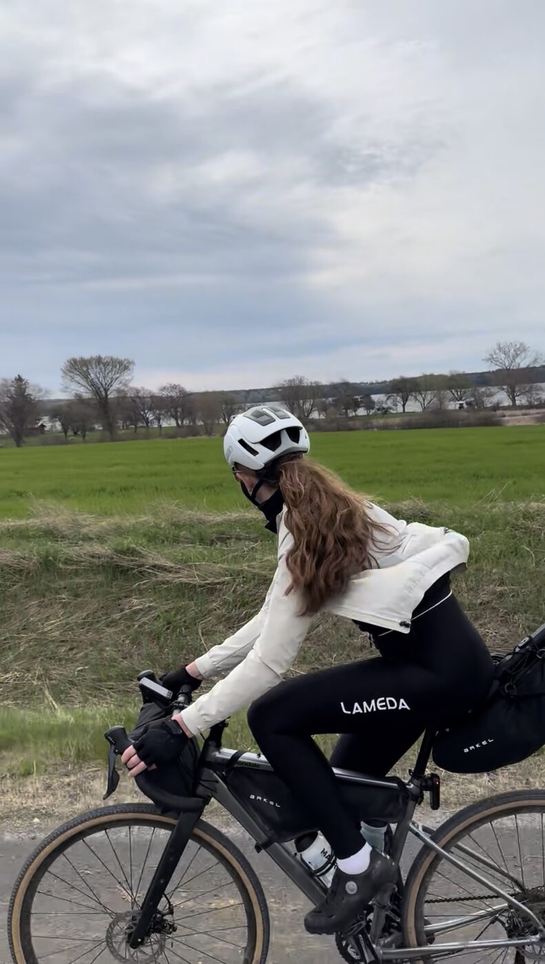 Bailey riding a farm road past a green field with the lake behind