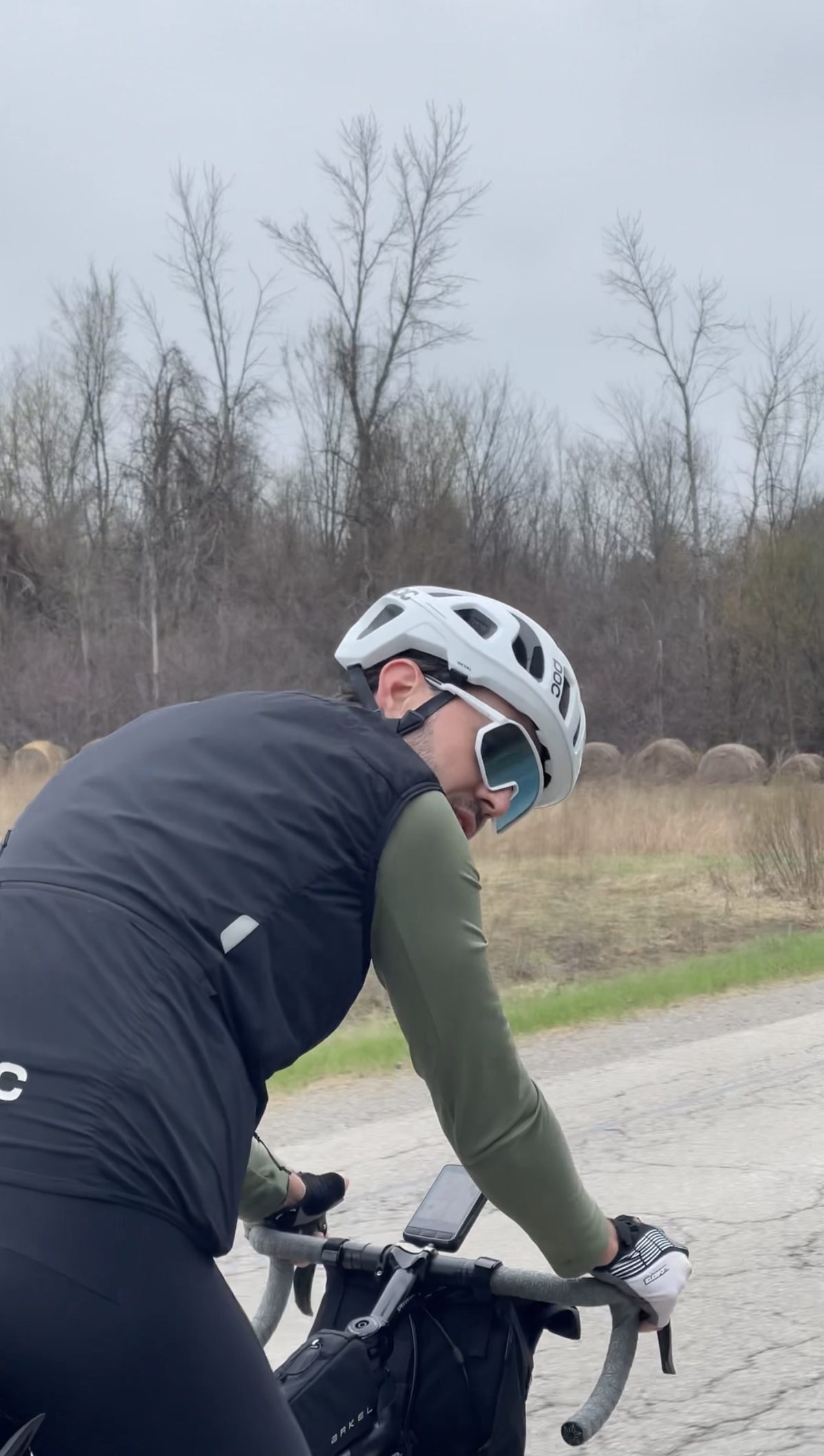 Francis riding a loaded bike along an open road past round hay bales in farm country
