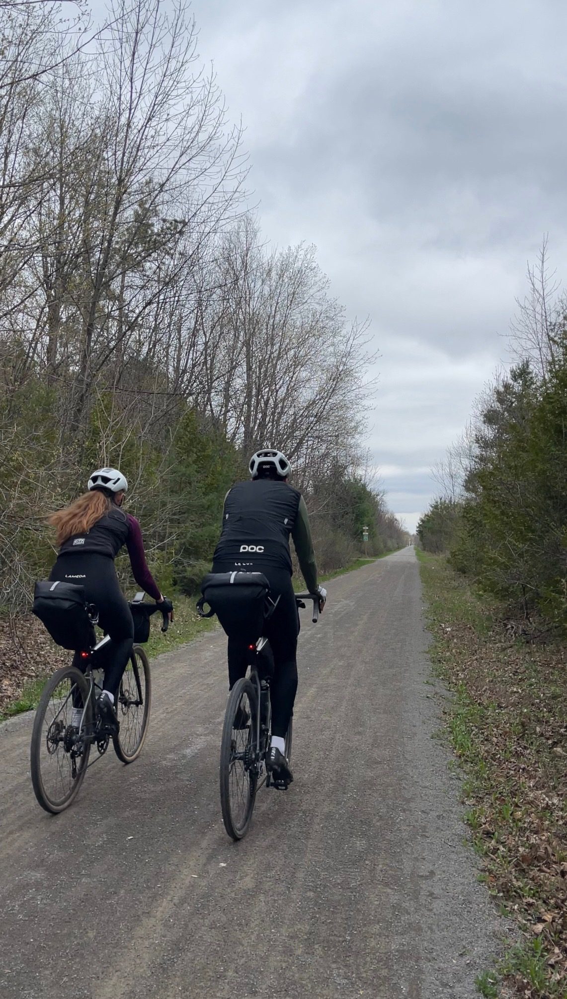 Francis and Bailey riding side by side on the tree-lined Osgoode-Leitrim rail-trail pathway toward Ottawa